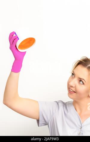 Ritratto di una beautician caucasica femmina che tiene un vaso di pasta di zucchero per zuccherare indossando guanti rosa su sfondo bianco Foto Stock