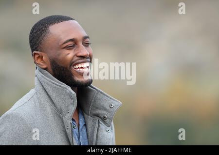 Uomo felice con pelle nera ridendo in montagna indossando giacca in inverno Foto Stock