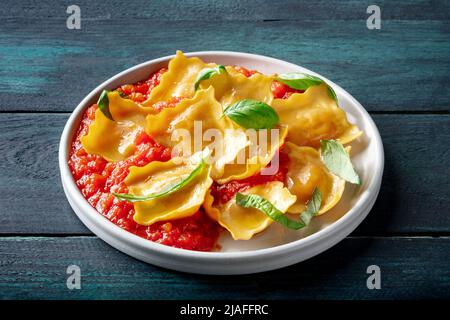 Ravioli con salsa di pomodoro e foglie di basilico fresco su un piatto, piatto di pasta italiana, su sfondo rustico scuro in legno Foto Stock