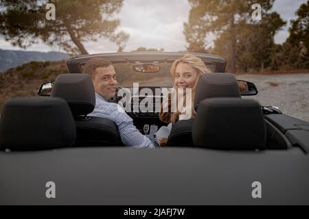 Coppia felice di uomo e donna seduti in un'auto convertibile e sorridente guardando indietro Foto Stock