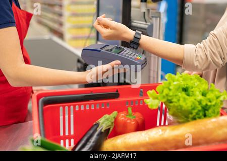 Giovane donna moderna che usa la tecnologia intelligente dell'orologio per pagare merci in moderno supermercato Foto Stock