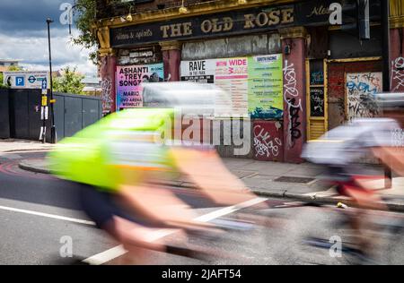 Due ciclisti che partecipano al RideLondon 2022 passano davanti ad un pub derelitto chiamato The Old Rose nel East End di Londra. L'evento si è tenuto per il primo tim Foto Stock