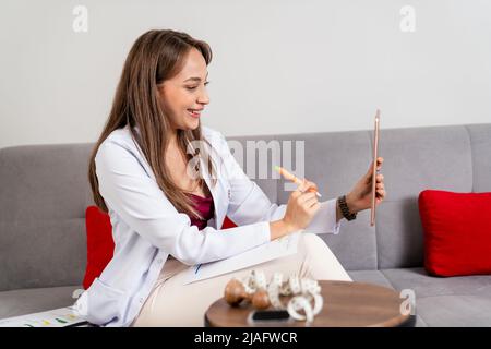 Giovane bel dietista sta consultando il suo paziente online nel suo tablet mobile. Foto di alta qualità Foto Stock