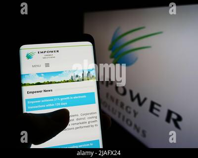 Persona che tiene lo smartphone con la pagina Web di Emirates Central Cooling Systems (Empower) sullo schermo davanti al logo. Concentrarsi sul centro del display del telefono. Foto Stock