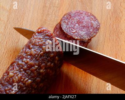 Il coltello taglia il salame su un asse di legno Foto stock - Alamy