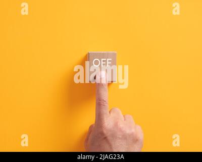 La mano maschio preme su un cubo di legno con la parola sopra. Pulsante di spegnimento, concetto di fine o finitura. Foto Stock