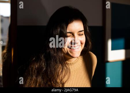 Giovane donna felice con gli occhi chiusi godendo la luce del sole a casa Foto Stock