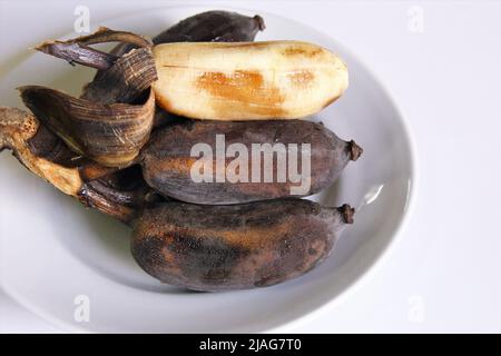 Sopra le banane mature su un piatto bianco, uno pelato. Foto isolate su sfondo bianco Foto Stock