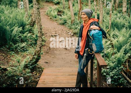 Una donna in un impermeabile e un cappello nei folti della foresta gode della freschezza dopo la pioggia Foto Stock