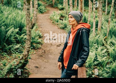 Una donna in un impermeabile e un cappello nei folti della foresta gode della freschezza dopo la pioggia Foto Stock