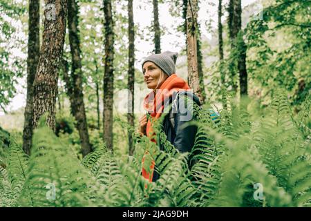 Giovane donna attiva escursionista in giacca e un cappello con uno zaino in un thicket di felci nella foresta Foto Stock