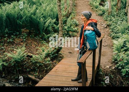 Una donna in un impermeabile e un cappello nei folti della foresta gode della freschezza dopo la pioggia Foto Stock