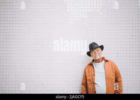 Ritratto di uomo anziano con cappello in piedi davanti alla parete bianca Foto Stock