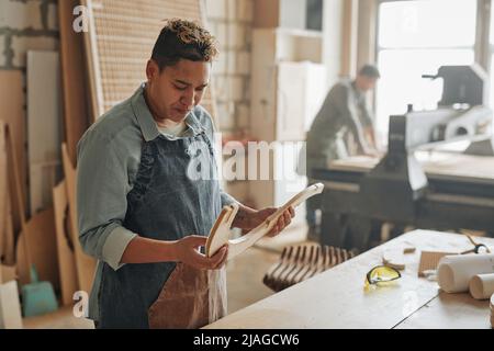 Ritratto di carpentiere femmina dai toni caldi che ispeziona parti di mobili in legno in laboratorio illuminato dal sole, spazio copia Foto Stock