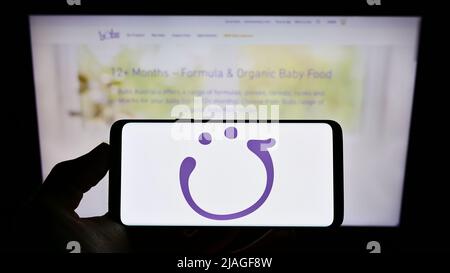 Persona che tiene il cellulare con il logo della società di nutrizione infantile Bubs Australia Limited sullo schermo di fronte al sito web. Mettere a fuoco sul display del telefono. Foto Stock