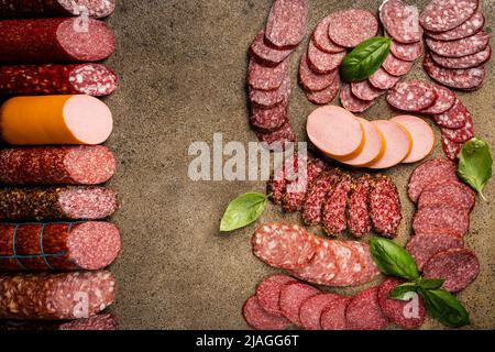 Set di diversi tipi di fette di salsicce con basilico e spezie su fondo di pietra. Vista dall'alto. Foto Stock