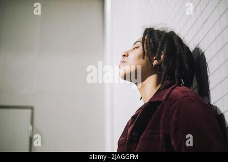 Persona non binaria con gli occhi chiusi appoggiati sul muro Foto Stock