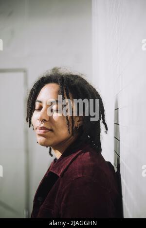 Genderqueer persona con gli occhi chiusi in piedi da muro durante la giornata di sole Foto Stock