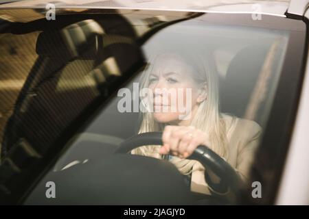 Curiosa donna d'affari che guida l'auto visto attraverso il parabrezza Foto Stock