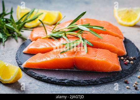 Pezzi di salmone crudo con spezie ed erbe su una tavola di ardesia, sfondo scuro. Foto Stock