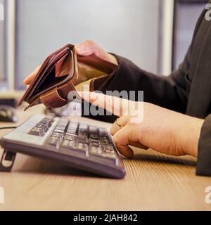 Un uomo d'affari con un portafoglio vuoto senza soldi nelle sue mani sta lavorando su una tastiera del calcolatore ad una scrivania dell'ufficio, primo piano Foto Stock