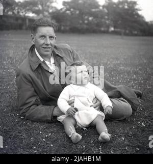 1950s, storico, un padre che giace sull'erba in un parco che tiene suo figlio neonato, Inghilterra, Regno Unito. Foto Stock
