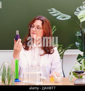 L'insegnante di sesso femminile esamina la reazione chimica di un reagente in un matraccio. Esperimenti scientifici in una classe di chimica scolastica Foto Stock