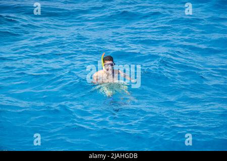 L'uomo africano è impegnato nello snorkeling. Un uomo in maschera e pinne nuota sul mare. Vista dall'alto. Hurghada, Egitto - Marzo 2022 Foto Stock