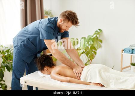 Ritratto di terapista maschile che dà indietro il massaggio alla giovane donna godendo sessione SPA Foto Stock
