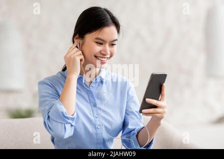 donna asiatica positiva che usa auricolari e smartphone Foto Stock