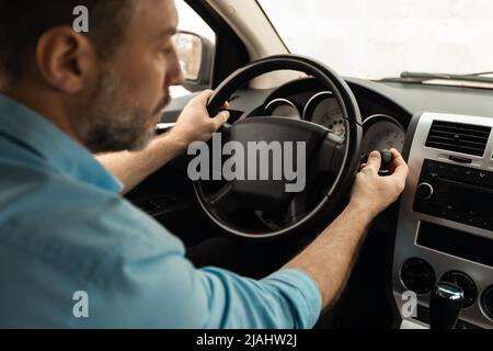 Uomo che guida una nuova auto in città, accendendo i tergicristalli Foto Stock