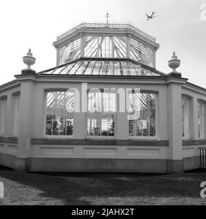 Richmond, Greater London, Inghilterra, maggio 18 2022: Royal Botanic Gardens Kew. Casa temperata con aereo che vola sopra. Monocromatico. Foto Stock