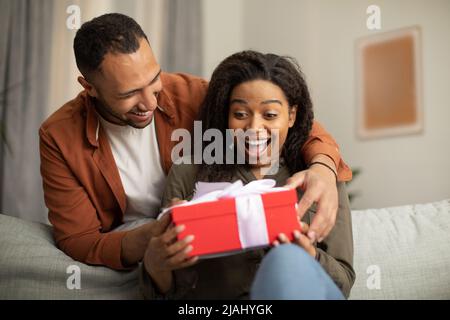 Felice marito nero che dà la scatola del regalo alla moglie a casa Foto Stock