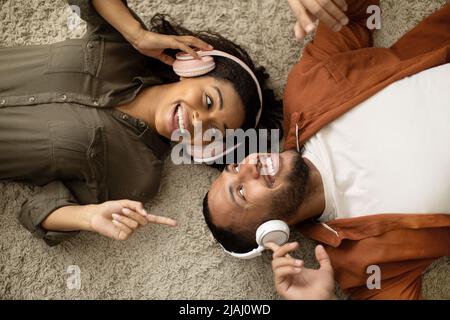 Happy African American Couple ascoltare musica indossando auricolari che si trovano al coperto Foto Stock