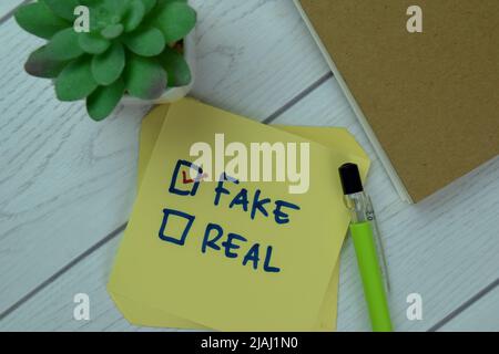 Concetto di falso o reale? Fake scrivere su note appiccicose isolato su tavola di legno. Foto Stock
