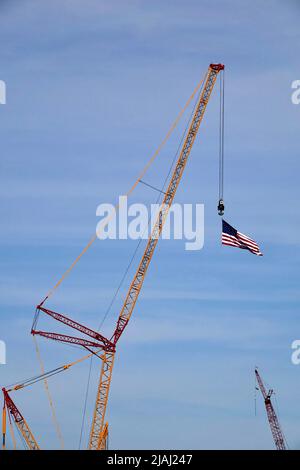 Una bandiera americana soffia nel vento mentre viene trascinata da una gru alta in un cantiere. Foto Stock