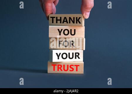 Grazie per la fiducia di Symbol. Parole di concetto grazie per la vostra fiducia su blocchi di legno su una bella tabella grigia sfondo. Mano dell'uomo d'affari. Busin Foto Stock