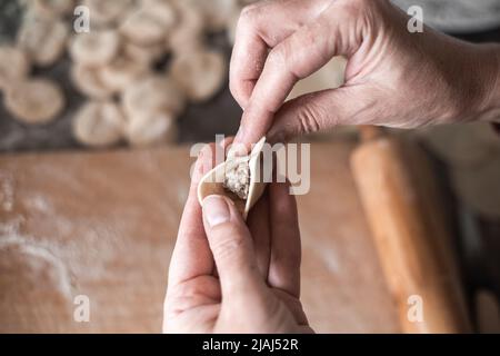 una donna scolpisce gnocchi con ripieno di carne. Cucinare un delizioso piatto russo. Foto Stock