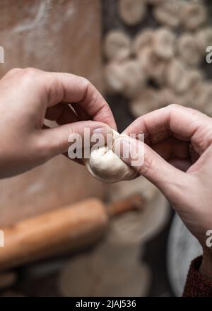 Una donna in cucina scolpisce gnocchi di pasta con ripieno di carne. Cucina deliziosi gnocchi fatti in casa. Foto Stock