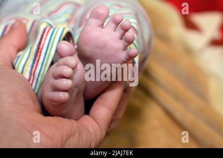 Un padre tiene il piede del bambino, le dita dei piedi del neonato in mano del genitore, i piedi del bambino neonato sul palmo del padre su uno sfondo sfocato, parenting, pazzi Foto Stock