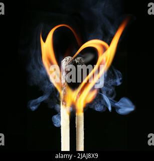 Due fiammiferi brucianti con fiamma a forma di cuore su sfondo scuro Foto Stock