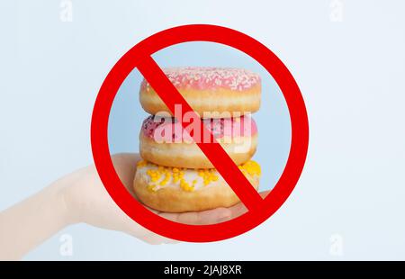 Mano con ciambelle dolci e segno di divieto su sfondo chiaro Foto Stock
