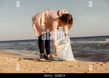 Donna volontaria e attivista pulizia spiaggia sabbiosa vicino al mare da rifiuti di plastica, rifiuti. Prelievo di bottiglie in borsa Foto Stock