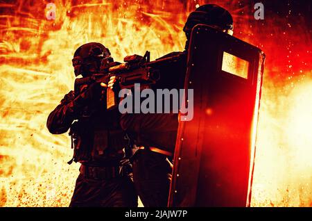 Gli ufficiali del team SWAT si proteggono dietro lo scudo balistico mentre si muovono attraverso un fuoco. Foto Stock