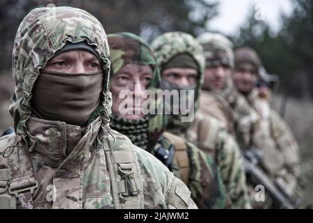 Gruppo di commandos esperti che indossano uniformi e maschere camouflage, in fila dietro il comandante. Foto Stock