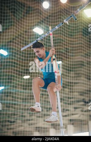 Palo che vaulting indoor - giovane fit sorridente uomo che salta appoggiandosi sul palo Foto Stock