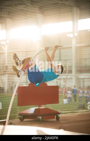 Pole Vault di allenamento nello stadio sportivo - giovane uomo in forma che salta sopra il bar Foto Stock