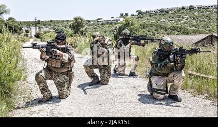 I soldati si inginocchiano e puntano le loro armi per osservare la zona con cautela e proteggersi a vicenda. Foto Stock