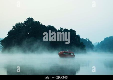 Una barca che galleggia in un nebbioso lago di nebbia Foto Stock