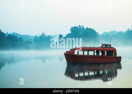 Una barca che galleggia in un nebbioso lago di nebbia Foto Stock